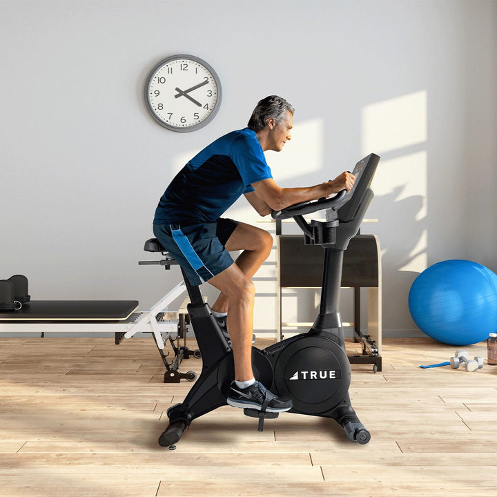 Man riding the True Fitness Performance Series Upright Bike in a bright home gym