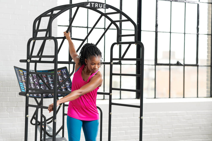 TRUE Stretch cage in use – woman doing a standing torso stretch in a bright studio